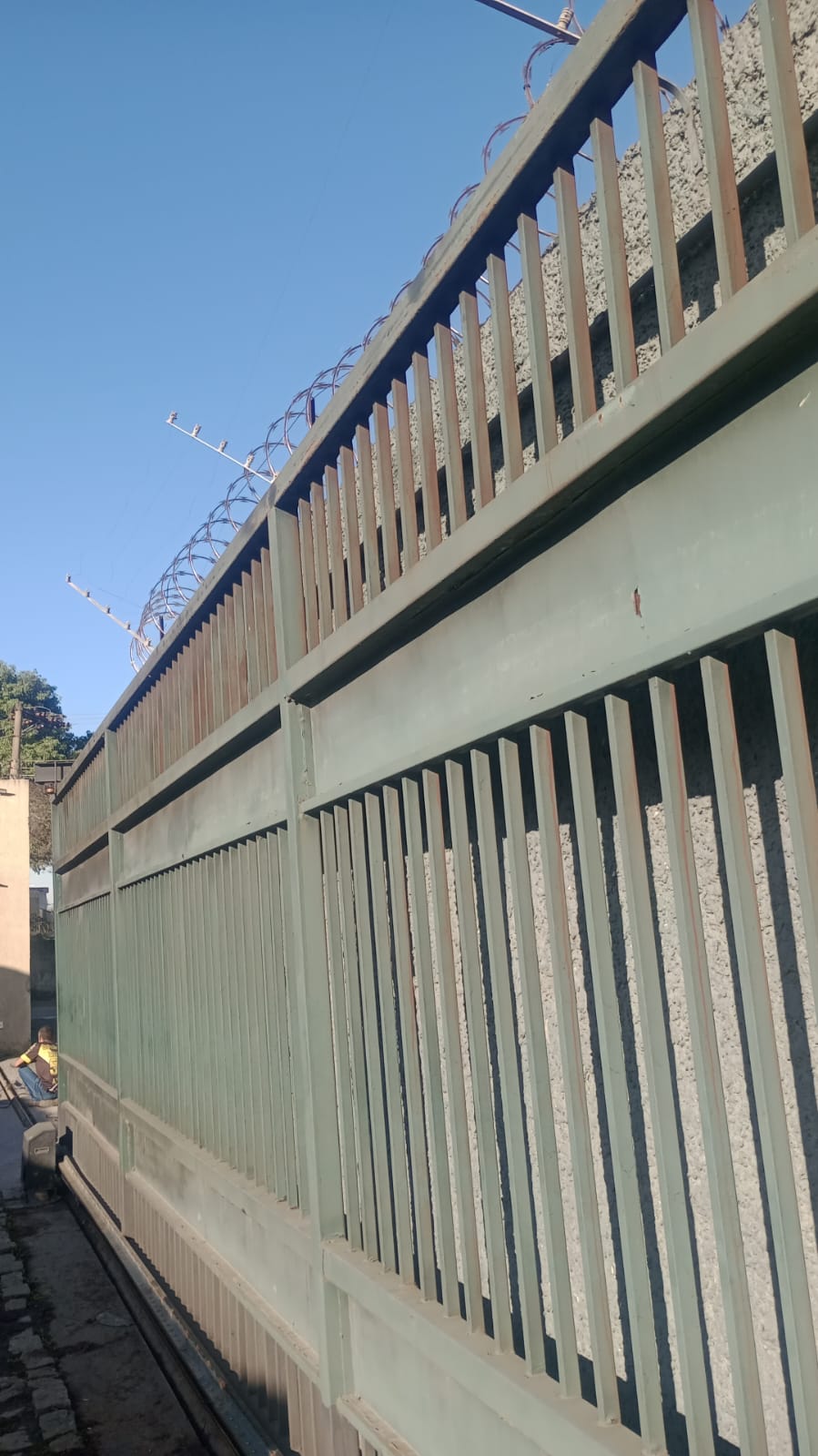 Portão de metal recém-pintado em verde com cerca concertina, demonstrando trabalho de pintura metálica