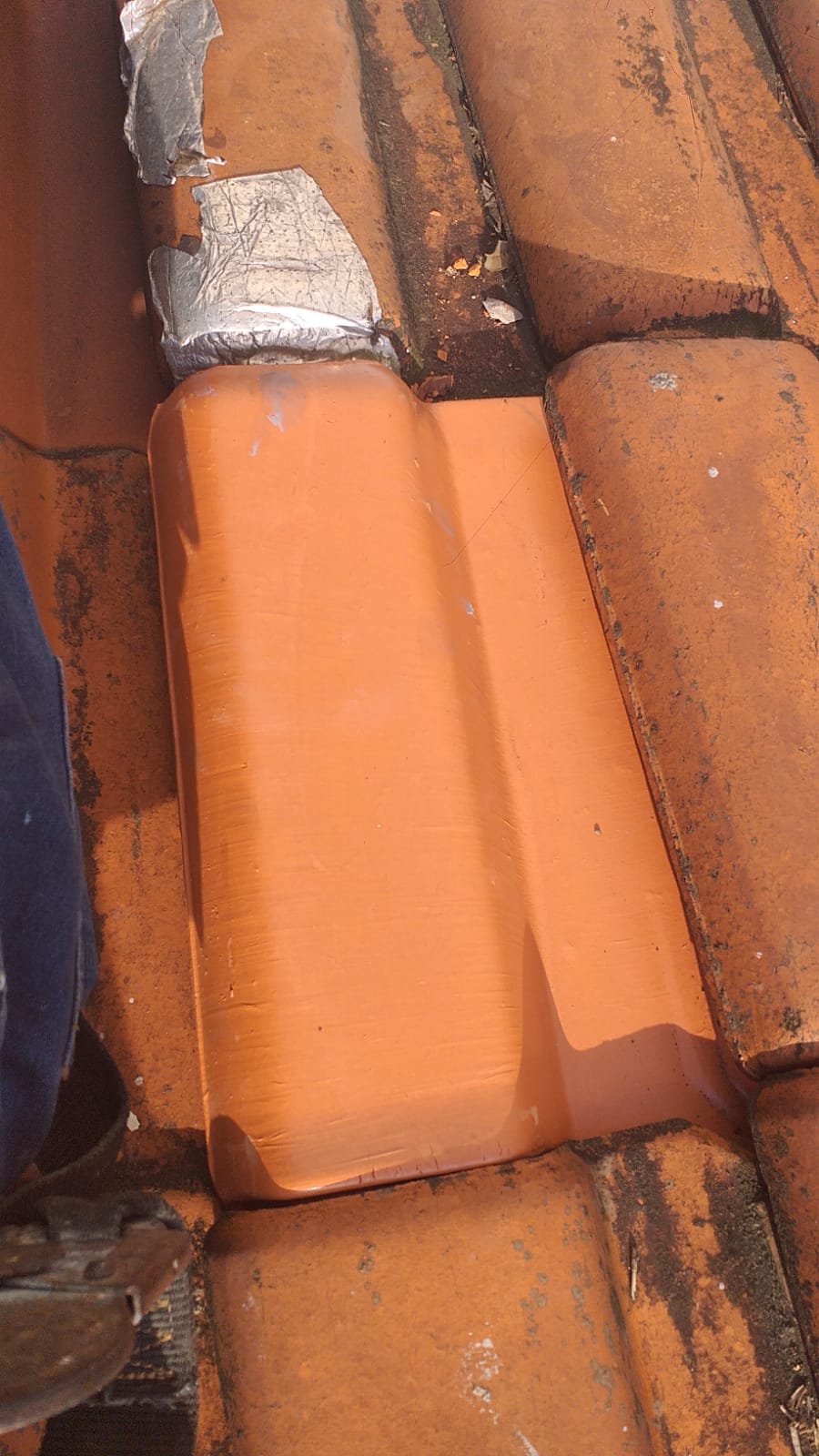 Telha cerâmica recém-pintada com tinta laranja sobre telhado de barro, evidenciando o serviço de pintura
